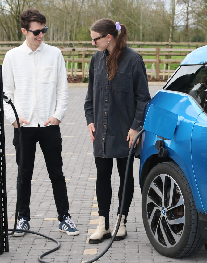 Company co-founders, one male and one female, stood outside charging a blue electric car